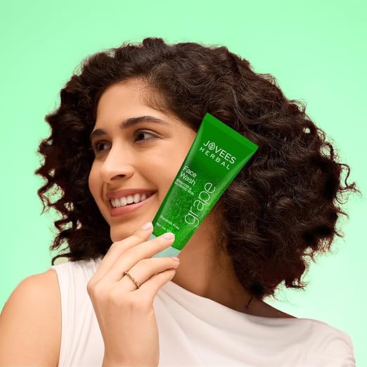 Woman holding Jovees Herbal Grape Fairness Face Wash against a light green background.